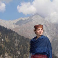 A picture of the writer, mountains standing tall behind her, somewhere in India.