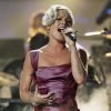 A picture of P!nk in a fuchsia dress, on stage at a concert, as she sings into a microphone and fog rolls in behind her.