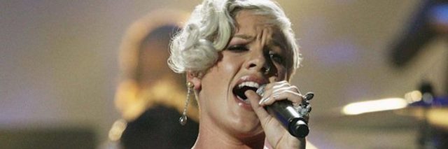 A picture of P!nk in a fuchsia dress, on stage at a concert, as she sings into a microphone and fog rolls in behind her.