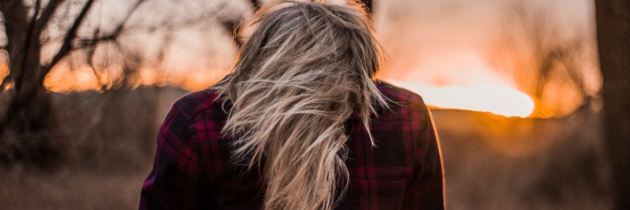 blonde haired woman with head down watching sunset