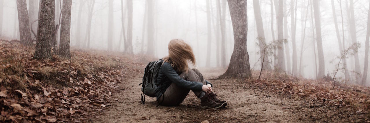 A woman sitting on a path in the woods, wearing a backpack, her hair is blurred