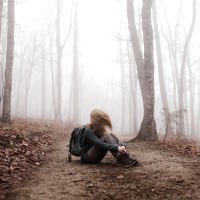 A woman sitting on a path in the woods, wearing a backpack, her hair is blurred