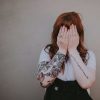 shy anxious young woman hiding face with hands with arm tattoos