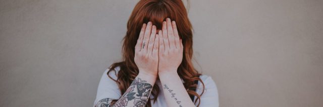 shy anxious young woman hiding face with hands with arm tattoos