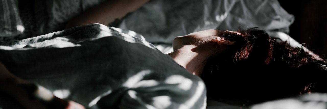 close up of woman lying in bed in patches of sunlight and darkness