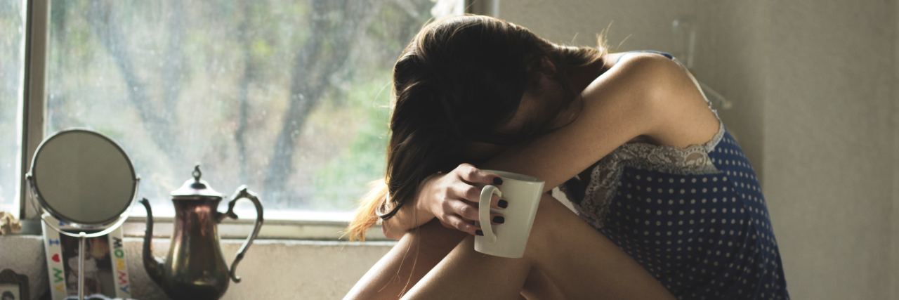woman sitting on bed with coffee cup and head buried in hands