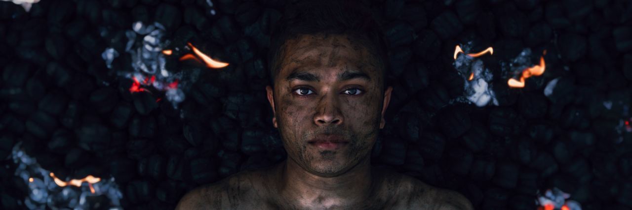 When Depression Invades Every Part of Your Day man laying in water with burning pieces of paper falling around him