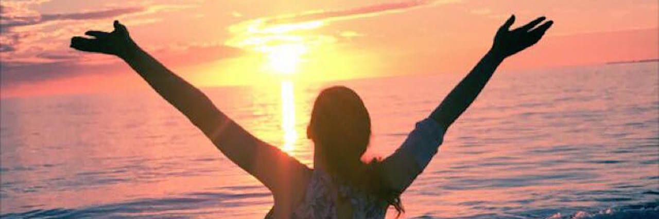 woman standing on a beach spreading her arms out at sunset