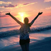 woman standing on a beach spreading her arms out at sunset