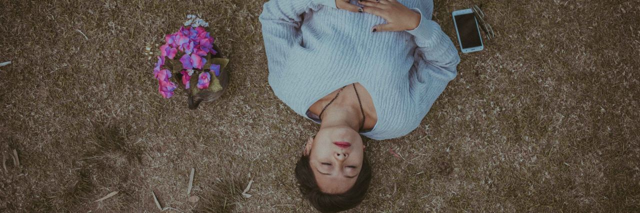 woman laying on ground next to flowers and phone