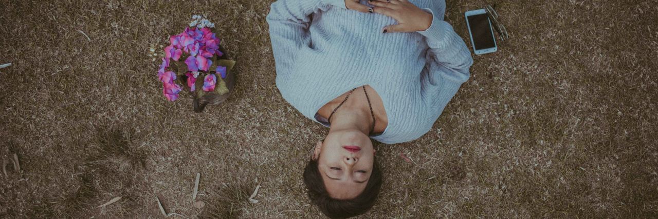 8 Phrases That Ease My Anxiety woman laying on ground next to flowers and phone