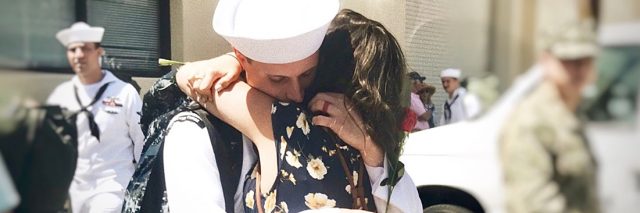 woman in flower dress and navy husband returning from deployment and embracing