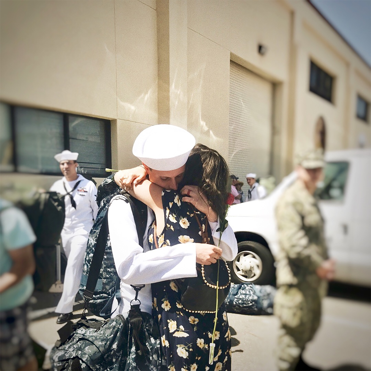 woman in flower dress and navy husband returning from deployment and embracing