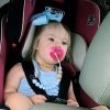 Mother driving with daughter in the back seat strapped in her carseat and with a pink pacifier. The little girl has Down syndrome.