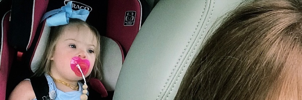 Specialists Don't Know Everything About Down Syndrome Mother driving with daughter in the back seat strapped in her carseat and with a pink pacifier. The little girl has Down syndrome.