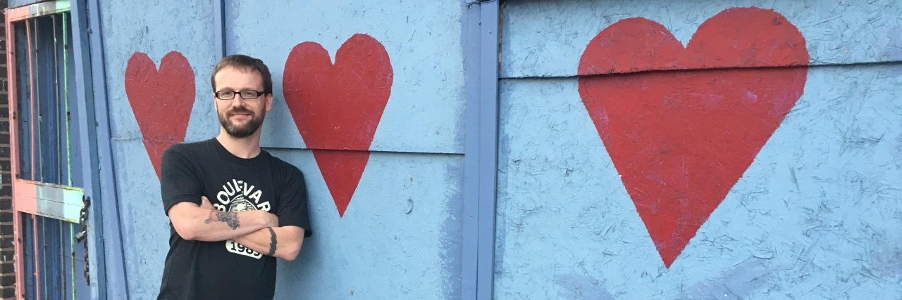 Autism and Meditation in Buddhism Daniel standing in front of a wall with hearts painted on it.