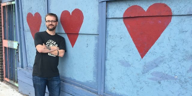 Daniel standing in front of a wall with hearts painted on it.