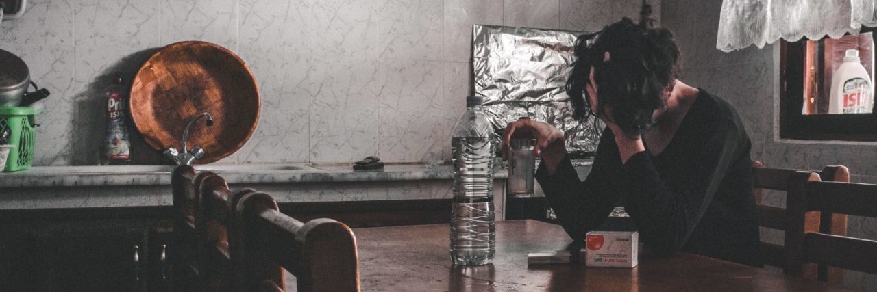 When Your Mental Illness Makes You Feel Out of Place in Your Own Home woman sitting at long table in dull room looking sick or upset