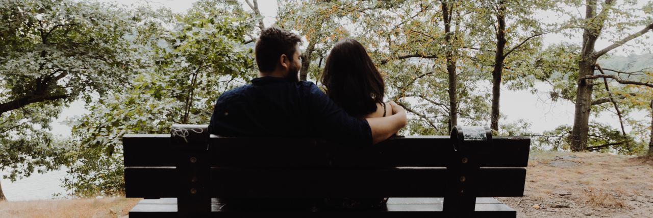 man and woman sitting on a bench looking off at the trees