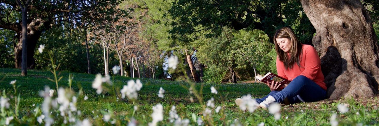 Self-Care Tips to Practice If You Experience ‘Spring Mania’ woman sitting on grass under tree reading book during spring