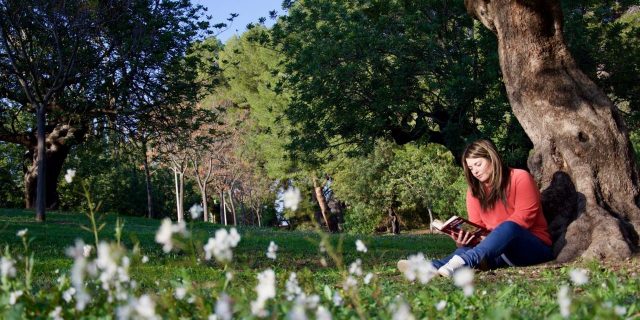 Self-Care Tips to Practice If You Experience ‘Spring Mania’ woman sitting on grass under tree reading book during spring