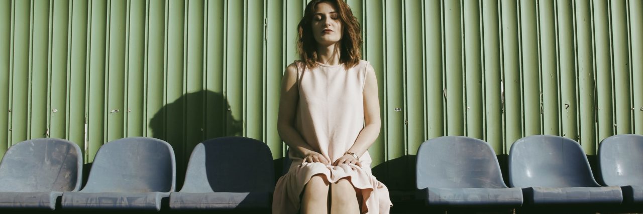 When Eating Disorders Become a ‘Competition’ woman sitting on chairs at stadium with closed eyes and corrugated metal behind her