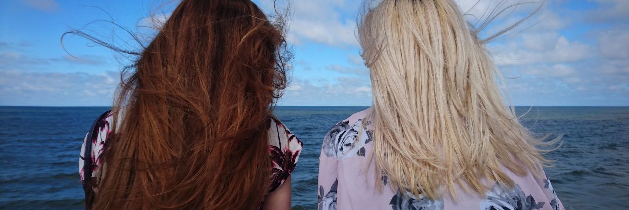 person of colour and white young woman talking by sea facing away from camera
