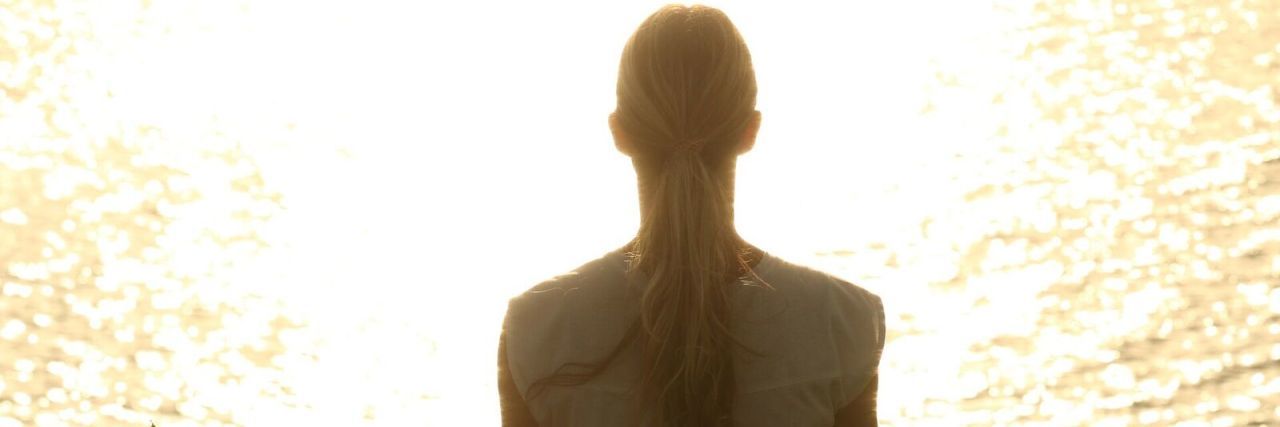 Emotional Effects of Scoliosis Woman meditating by a lake.