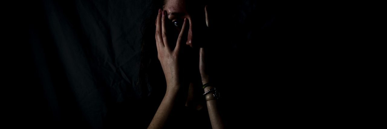 woman in darkness with hands covering her mouth