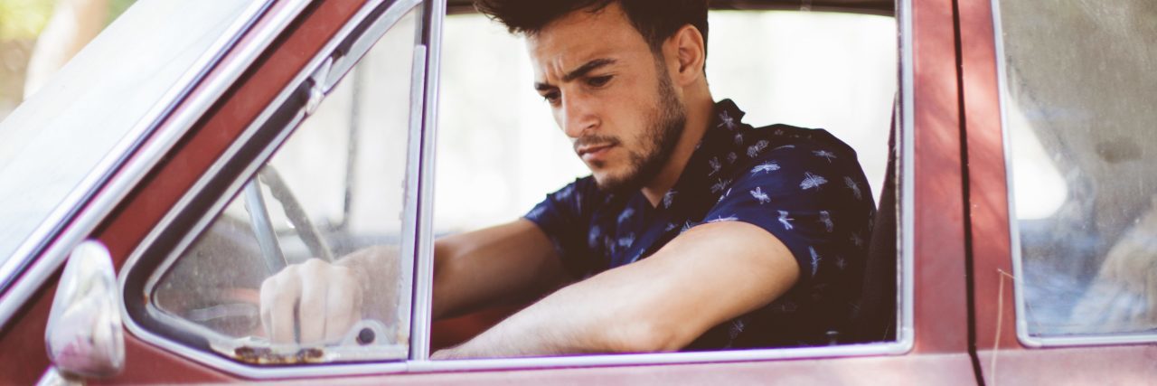 young man behind driver sear of red vintage car