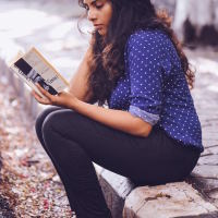 indian woman sitting on a curb reading a book