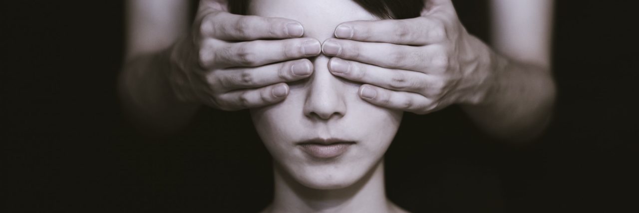 monochrome image of woman having her eyes covered by someone unseen from darkness