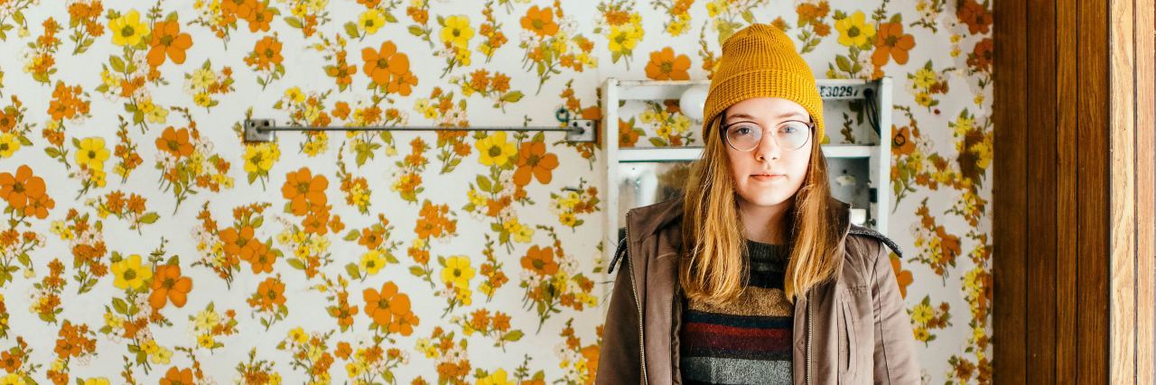 3 Things I Do Regularly to Regain Power Over My Eating Disorder woman with hat and glasses stands in bathroom with floral wallpaper