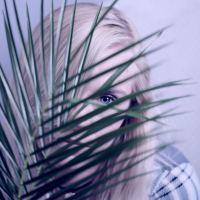 young girl with blonde hair and blue eyes hiding behind plant