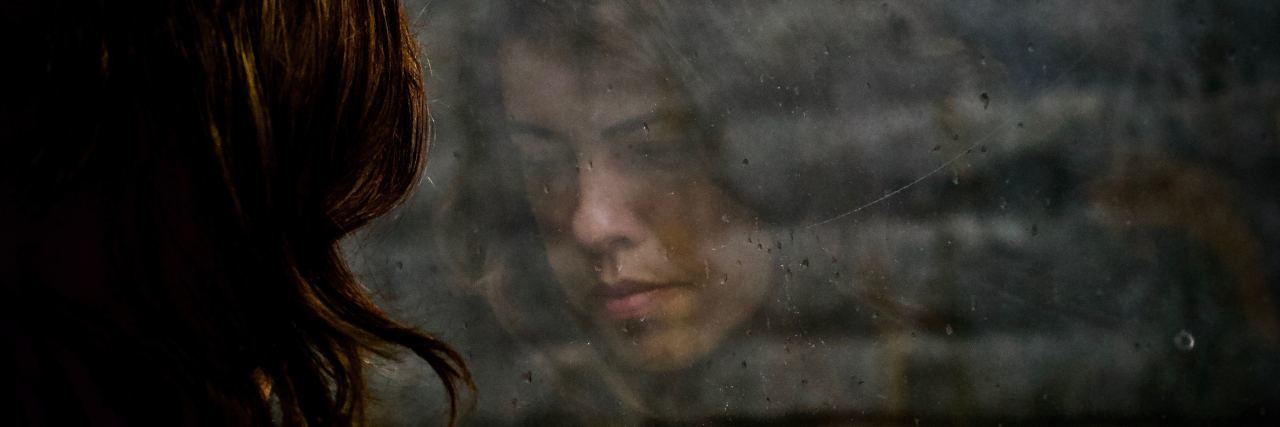 The Sadness of Leaving Your Therapist young woman and her reflection in window with brick wall looking sad