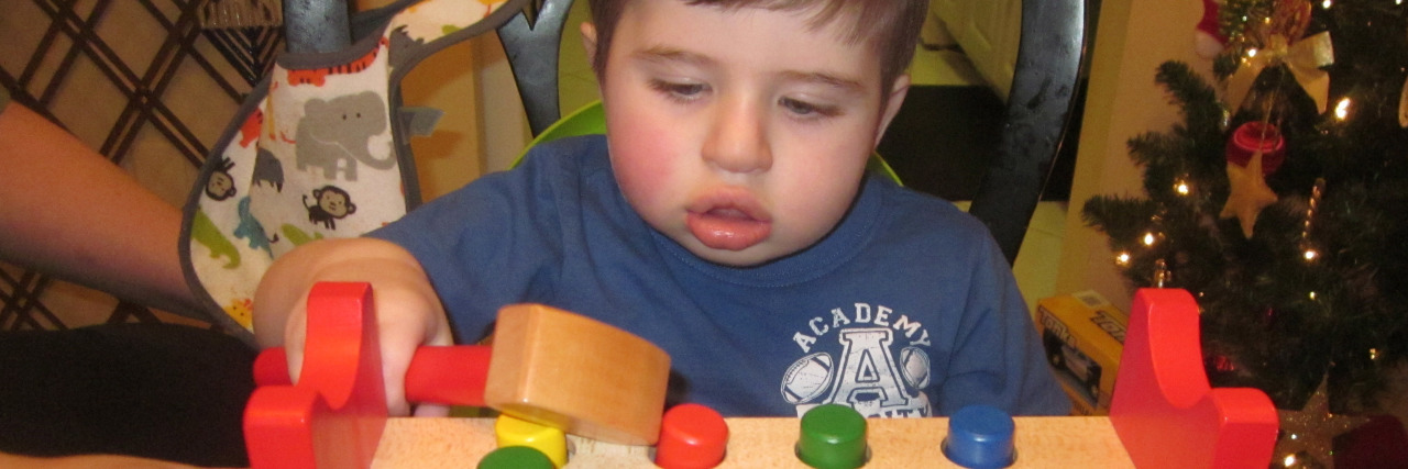 Little boy sitting in front of peg toy trying to hold mallet.