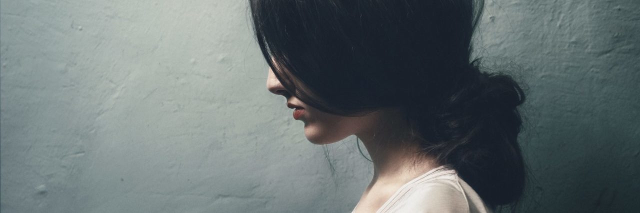 How to Ask Someone With Depression If They Are OK profile of young woman with hair covering face against dark wall