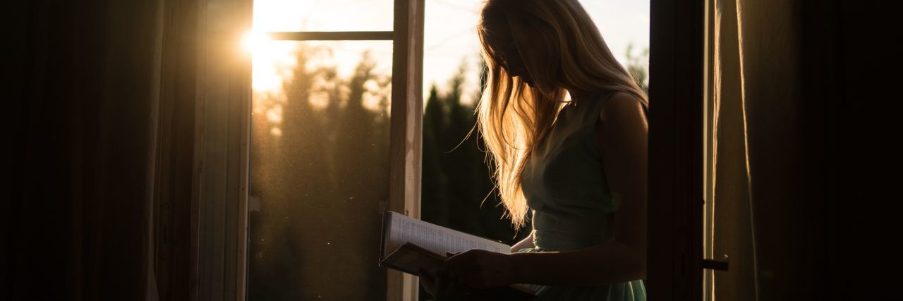 woman reading book by sunset on window ledge