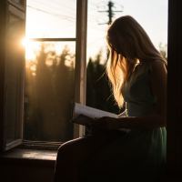 woman reading book by sunset on window ledge
