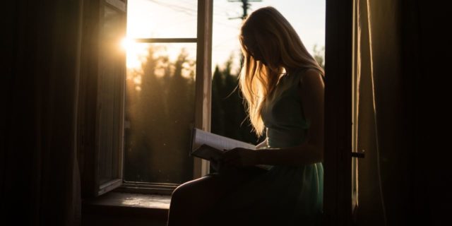 woman reading book by sunset on window ledge