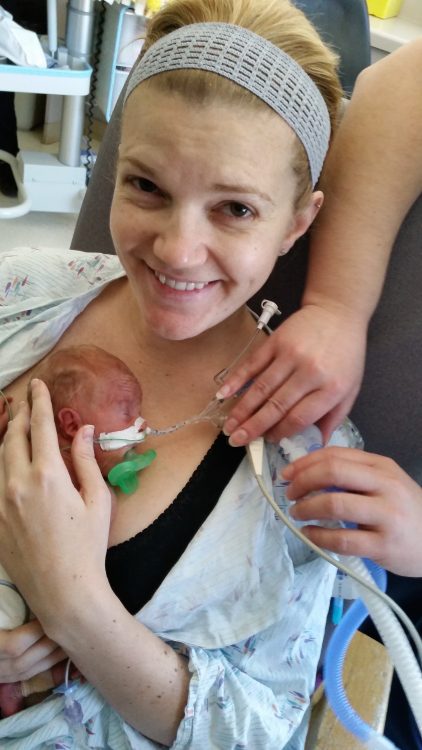 mom in nicu looking up at camera and smiling as she holds her preemie baby against her chest