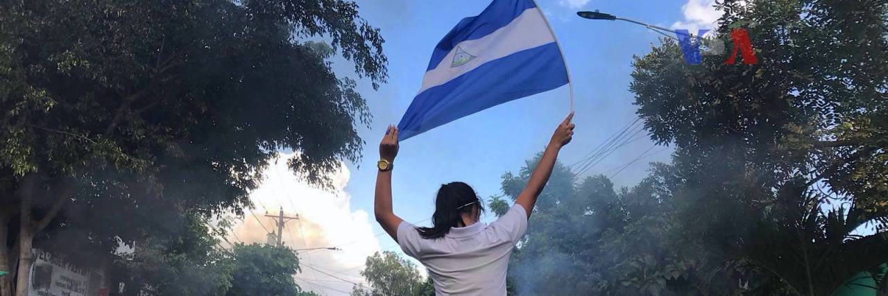 woman and nicaraguan flag at protests with burning barricade
