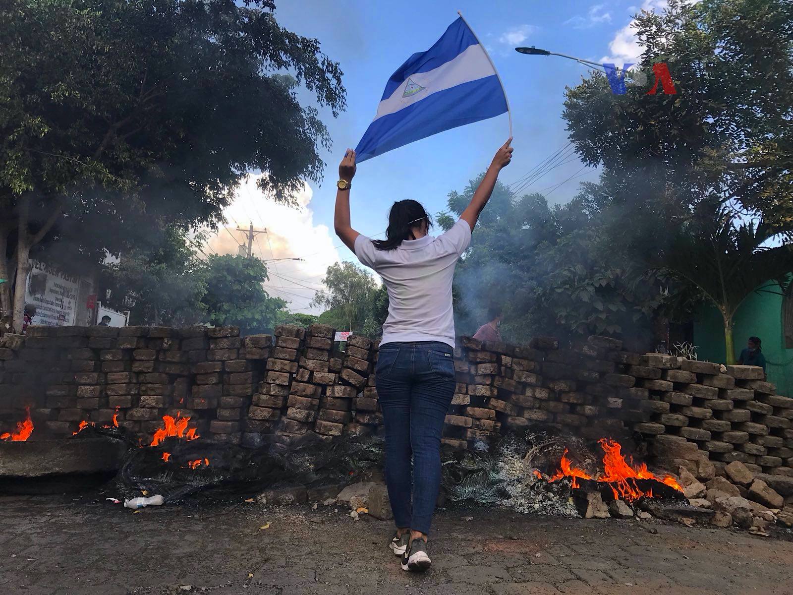 woman and nicaraguan flag at protests with burning barricade