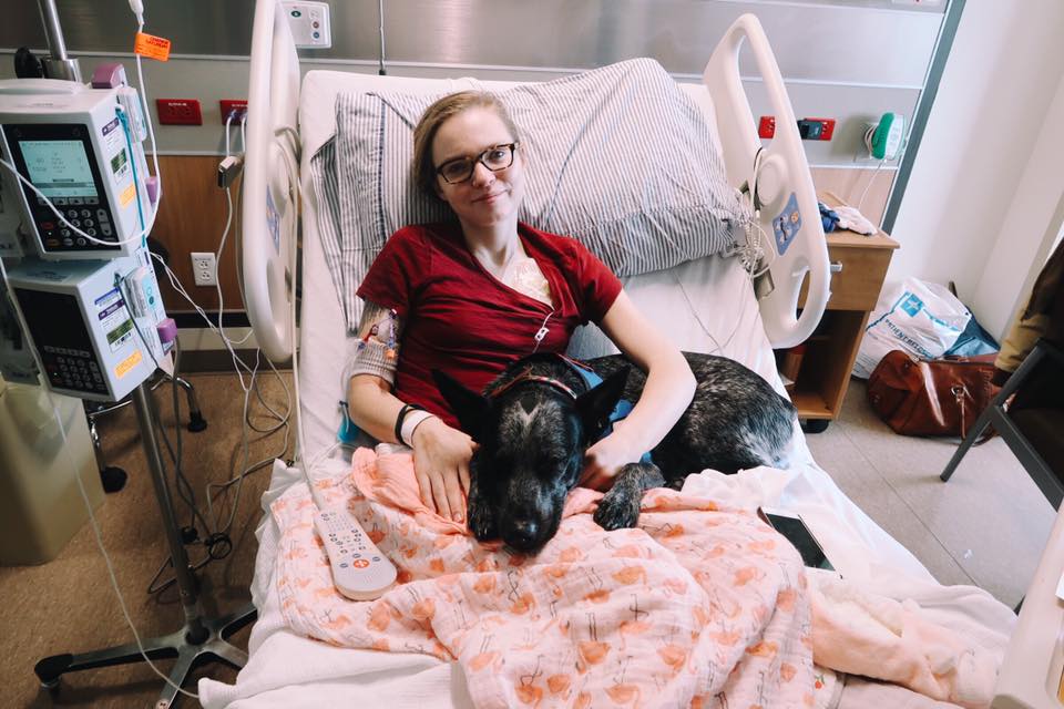 woman lying in a hospital bed with her service dog