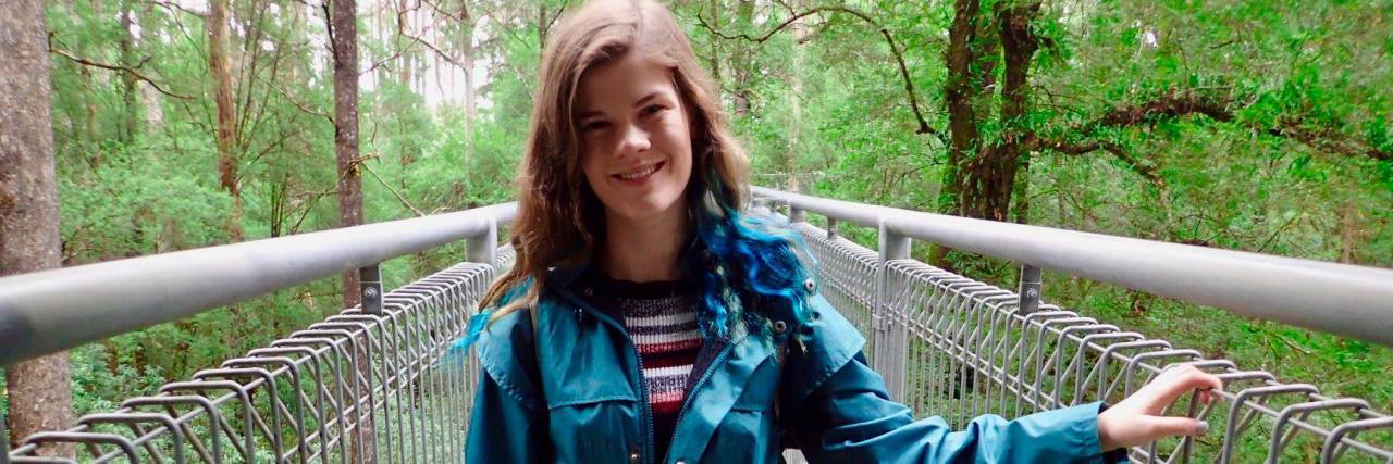 How I've Found Closure With Fibromyalgia A picture of the writer on a bridge, surrounded by greenery.