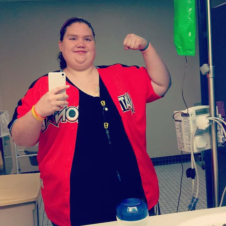 woman taking a selfie in a mirror next to her IV stand and flexing her bicep