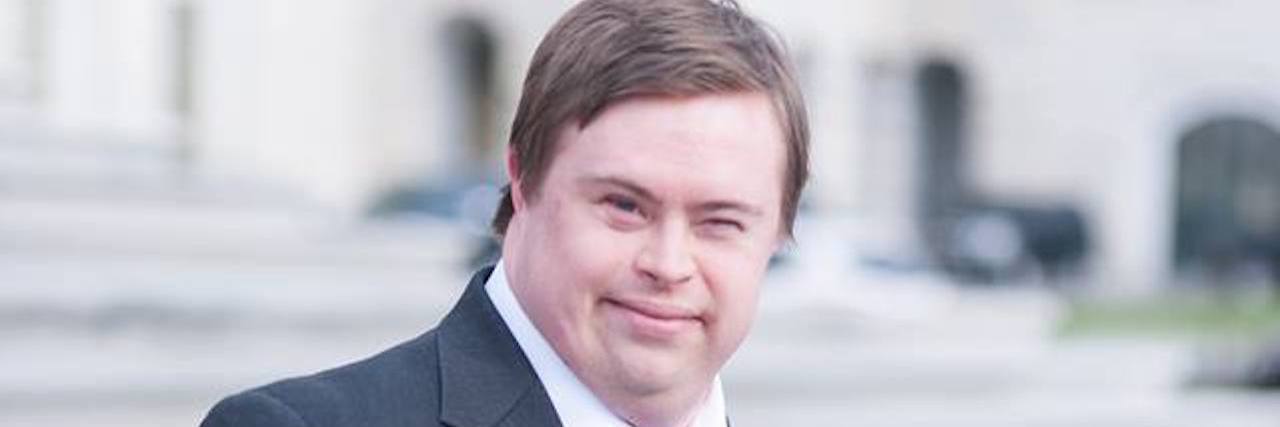 Adrian Forsight wearing a suit standing before government building with little girl with Down syndrome