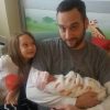 Image of dad holding newborn baby girl at the hospital with older daughter smiling by his side