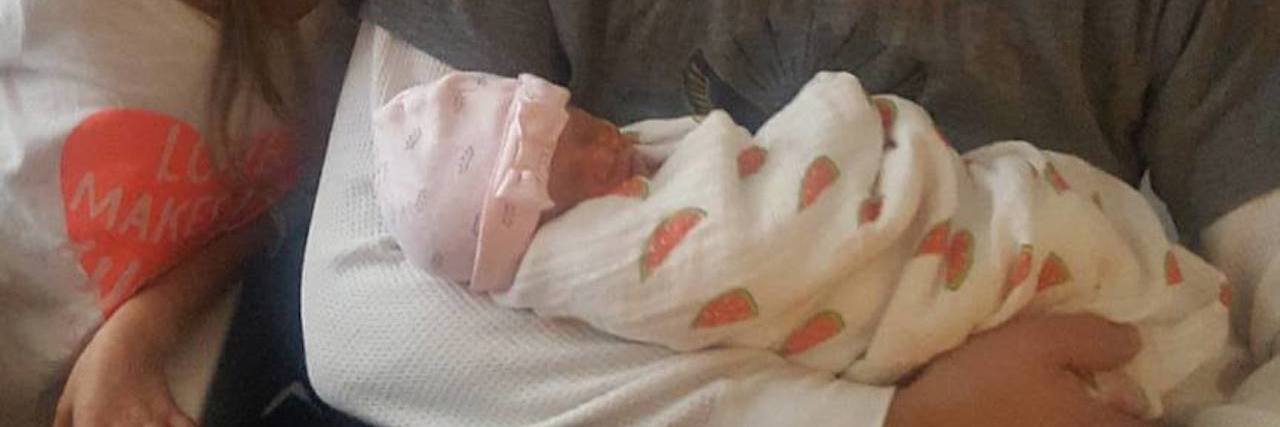 Image of dad holding newborn baby girl at the hospital with older daughter smiling by his side