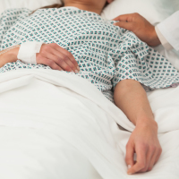 sick patient lying in hospital bed with a hand on her shoulder